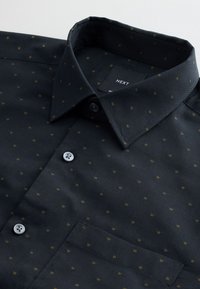 Dunkelblauses Hemd mit Kragen, das ein dezentes Muster aus kleinen goldenen Punkten aufweist. Es ist mit Knöpfen und einer Brusttasche ausgestattet. Das Material wirkt glatt.