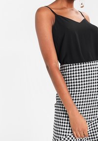 Donna che indossa un top nero senza maniche infilato in una gonna a vita alta a scacchi bianco e nera, con orecchini a cerchio visibili.