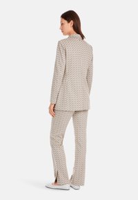 Beige suit with geometric pattern, featuring a fitted blazer and matching flared pants, with slits at the hems. Material appears textured.