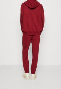Maroon hoodie with attached hood and matching sweatpants. Soft material, relaxed fit, elastic cuffs, and seams, paired with chunky beige sneakers.