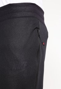 Närbild av svarta Nike Air sweatpants-fickan med dragkedja och märkesdragband, som visar texturerat tyg och midjeband.