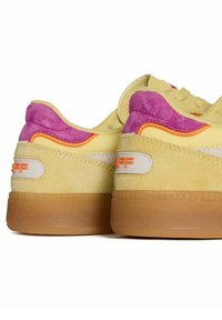 Las zapatillas de ante amarillas cuentan con acentos en rosa y naranja, una suela de goma texturizada y un detalle del logo en el talón. Diseño de bloqueo de color distintivo.