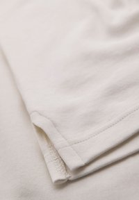 Ljusbeige bomullstyg med en mjuk textur. Har en vikt kant och sydda sömmar, vilket visar ett enkelt och rent design.