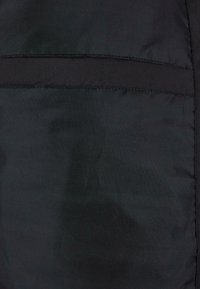 Černá péřová bunda s hladkým povrchem. Obsahuje horizontálně šitý šev a skryté kapsy, což vytváří elegantní vzhled.