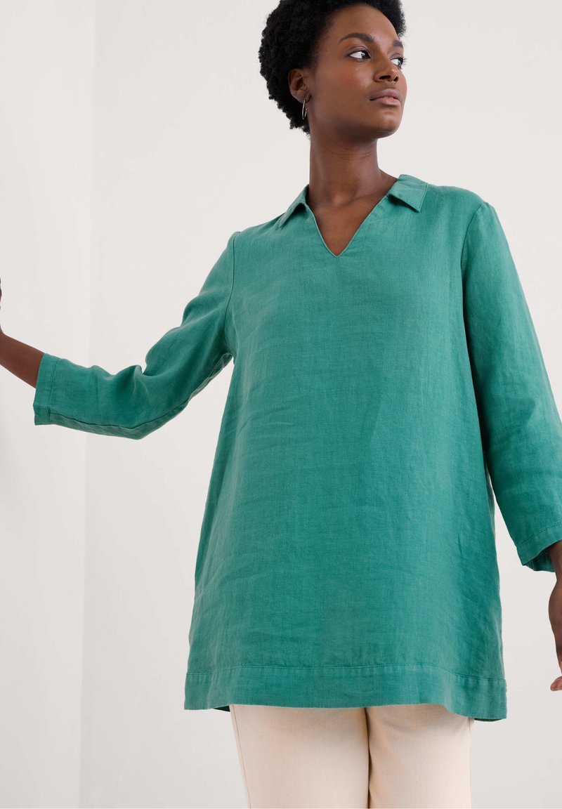 Zaļš lina tunika ar V-veida kakla izgriezumu, trīs ceturtdaļu piedurknēm un brīvu piegriezumu. Iezīmē vienkāršu dizainu ar tīrām līnijām.