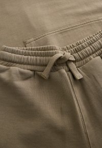 Beiga mjukisbyxor gjorda av mjukt bomullsmaterial. Har ett elastiskt midjeband med snöre och en sidoficka. Slät textur.