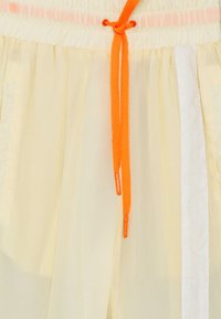 Helle gelbe Shorts mit einem elastischen Bund, ausgestattet mit einer orangefarbenen Kordel. Enthält Taschen und ein Design mit weißen Seitenpaneelen.