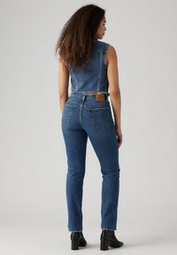 Conjunto de chaleco y jeans de mezclilla en azul oscuro. El chaleco presenta un diseño corto con dobladillo deshilachado, mientras que los jeans tienen un ajuste clásico con bolsillos traseros.