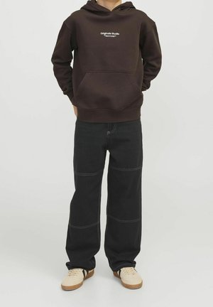 Ruskokapucnisvetšerslisavtorba v sprednju žep in belim logotipom; v kombinaciji z ohlapnimi črnimi hlačami z kontrastnim šivom in bež čevlji.