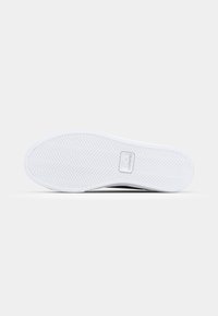 Fekete cipőtalp halszálka mintázattal, fehér gumiéllel és a Lacoste logóval a közepén. Simább felület és ívelt forma.
