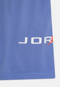Plava mrežasta majica s perforiranom teksturom. Bijeli logo "JORDAN" s crvenim naglaskom. Ravni rub i šivani krajevi. Lagana tkanina.