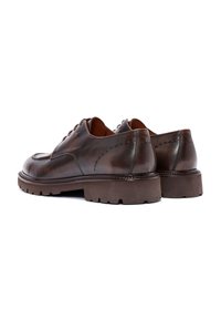 Zapatos de cuero marrón con un acabado suave, puntera redondeada y suela resistente. Presenta costuras decorativas a lo largo de los laterales y un tacón robusto.