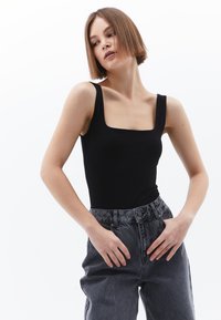 Body noir à col carré avec larges bretelles, associé à un pantalon en denim gris taille haute, présentant une coupe décontractée et un bouton avant visible.
