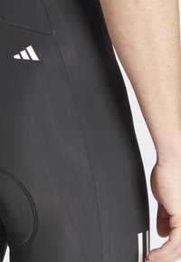 Collant sportivi neri con una texture liscia e affusolata. Logo e strisce bianche di spicco sui lati. Primo piano che mostra la vestibilità e i dettagli delle cuciture.