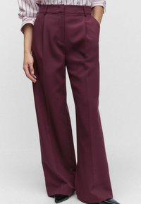 Wide-leg trousers in a deep burgundy color, made from a smooth fabric. Features belt loops and subtle front pleats.