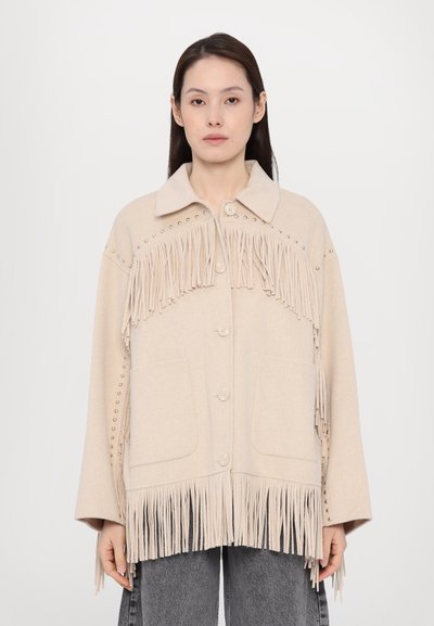 Beige Wolljacke mit Fransenverzierungen, Druckknöpfen und aufgesetzten Taschen. Mit metallischen Nieten entlang der Schultern und Ärmel.