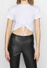 Vit ribbad cropped top med korta ärmar, med en samlad framdel och knytning vid fållen, matchad med höga svarta läderleggings.