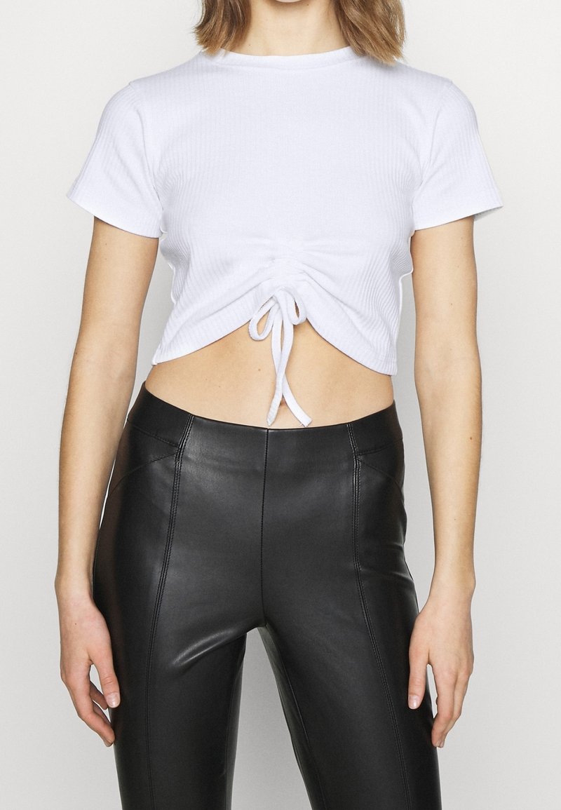 Vit ribbad cropped top med korta ärmar, med en samlad framdel och knytning vid fållen, matchad med höga svarta läderleggings.