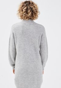 Robe-pull gris tricotée avec un col montant, un tricot côtelé texturé et des manches longues, s'étendant jusqu'à la mi-cuisse.