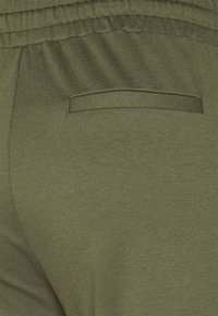 Jogging en olive en tissu doux et texturé, avec une taille élastique et une poche arrière discrète pour le rangement.