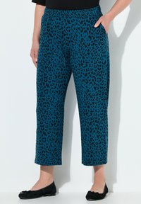 Türkise Leopardenmuster-Hosen mit einem dehnbaren Bund, cropped Länge und Seitentaschen. Kombiniert mit schwarzen Ballerinas und einem schwarzen Oberteil.