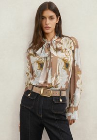 Beezhnahast ja valgest lillemustrist pluus, millel on seotav kaelusdetail ja pikad varrukad. Sobitatud tumeda teksariidest kõrge vöökohaga pükstega ning hele vöö.