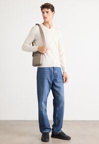 Maglione beige chiaro a scollo a V, jeans blu a gamba dritta, sneakers nere e una piccola borsa a tracolla grigia con il logo "BOSS" in un design minimalista.