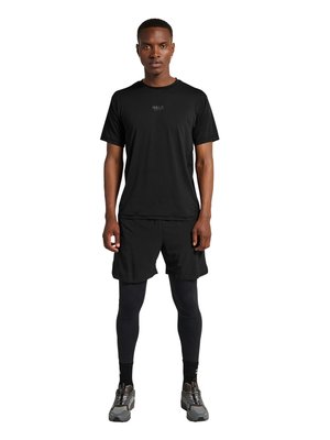 Mężczyzna stoi, ubrany w czarną koszulkę z krótkim rękawem, czarne spodenki na czarnych legginsach, czarne skarpetki i szare buty do biegania na białym tle.