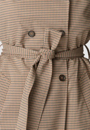 Manteau ceinturé à carreaux marron, noir et crème avec de grands boutons et des poches à rabat sur un fond uni.