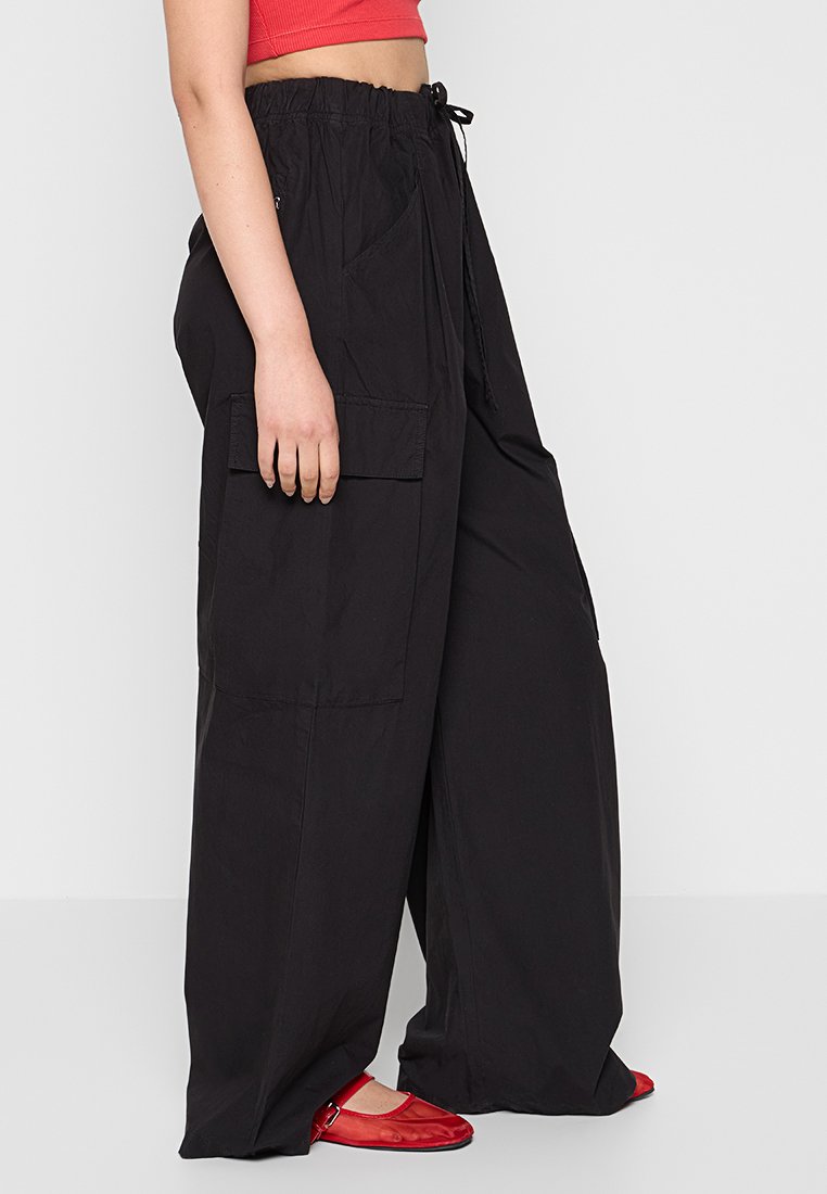 Pantaloni cargo neri a gamba larga con vita elastica, coulisse e tasche laterali. Texture liscia e vestibilità rilassata.