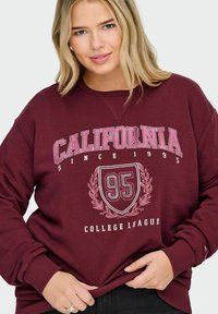 Burgundijas džemperis ar tekstu "California Since 1995" un vairoga grafiku ar "95" pērļu dizainā; ribināta apkakle un aproces.
