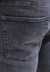 Nahaufnahme von dunkelgrauem Denimstoff, der die Gesäßtasche und die Nähte einer Jeans zeigt.