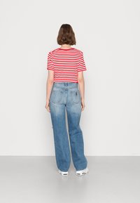 T-shirt cropped com riscas vermelhas e brancas, de mangas curtas, combinada com jeans de perna larga em azul claro, que apresentam bolsos nas costas e um leve desbotamento.