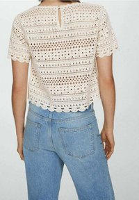 Kremowy top na szydełku z krótkimi rękawami, okrągłym dołem i dekoltem w kształcie łezki z tyłu, w połączeniu z jasnoniebieskimi dżinsami o wysokim stanie.