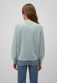 Helles blaues Strickpullover mit einem strukturierten geometrischen Muster auf der Rückseite, mit langen Ärmeln und einem runden Halsausschnitt.