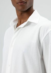 Witte overhemd met zachte textuur, omgeslagen kraag en sluiting met één knoop. Heeft een comfortabele pasvorm en minimalistische designdetails.