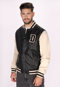 Schwarze Leder-Collegejacke mit cremefarbenen Ärmeln, gestreiftem Rippkragen und -bündchen sowie einem großen, auf die Brust gestickten Buchstaben "D".