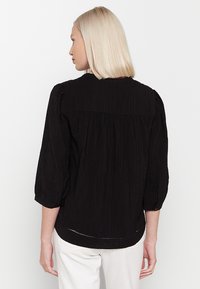 Czarna, teksturowana bluzka z rękawami do trzech czwartych, marszczonymi ramionami i zaokrąglonym dekoltem. Posiada subtelny detal na dolnym brzegu i luźny krój.