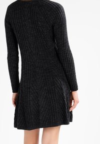 Una donna che indossa un vestito grigio scuro a coste, visto di spalle, che mette in risalto la texture e il design del capo.
