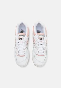 Weiße Sportschuhe mit rosa Akzenten, ausgestattet mit einem glatten Leder-Obermaterial, runder Zehenpartie, Schnürdesign und perforierten Details für Atmungsaktivität.