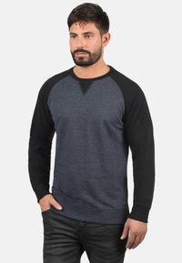 Felpa blu scuro con maniche raglan nere, dotata di scollatura a girocollo, texture morbida e una piccola etichetta del marchio in basso.