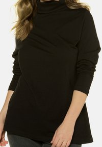 Black long-sleeve turtleneck made of soft fabric, featuring a relaxed fit and side ruching details, providing a smooth texture and silhouette.