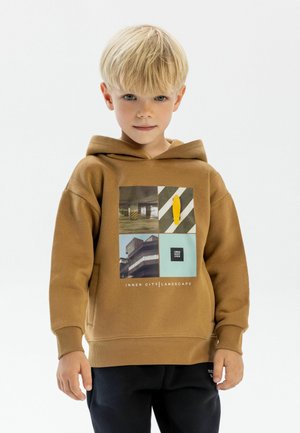 Brown hoodie made of soft fabric featuring graphic print with urban themes. Cuffs and hem are ribbed. Paired with dark pants.