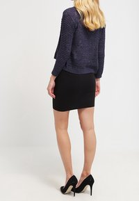 Suéter de punto azul marino con patrón texturizado, combinado con una falda corta negra ajustada y zapatos de tacón alto negros. Tejidos lisos y ajustados.