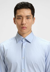 Camicia a maniche lunghe a righe blu chiaro con colletto a punta, dotata di bottoni bianchi e di un tessuto liscio e morbido al tatto.