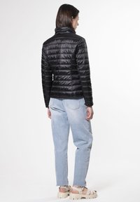 Chaqueta de plumas negra con un diseño ajustado, textura acolchada y cuello alto. Combinada con jeans de color azul claro y sandalias de plataforma beige.