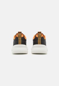 Schwarze Sportschuhe mit orangefarbenen Mesh-Akzenten, einer strukturierten weißen Sohle und einem vertikal gestreiften Zuglasche auf der Rückseite.