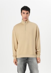 Felpa beige con zip a un quarto, colletto alto e polsini a costine. Realizzata in tessuto morbido, presenta un discreto logo sul petto.
