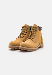 Bottines en nubuck beige avec des accents marron, dotées d'œillets en métal, de lacets et de semelles en caoutchouc robustes. Texture lisse et construction solide.