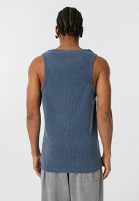 Blauw ribgebreid tanktop met een ronde halslijn en een rauwe zoom. Het materiaal lijkt zacht; het ontwerp heeft brede armsgaten voor comfort.